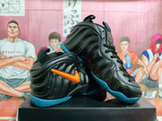 Angled view of the black Nike Foamposite pair displaying the orange side branding, sculpted upper and blue outsoles.