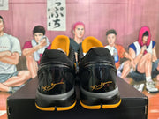 Rear view of black and yellow basketball sneakers showing glossy heel panels, black collars and yellow outsole accents on a shoebox.