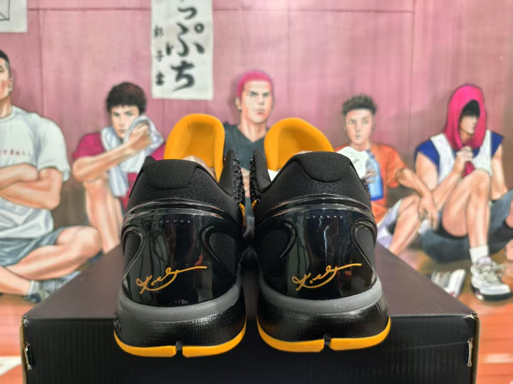 Rear view of black and yellow basketball sneakers showing glossy heel panels, black collars and yellow outsole accents on a shoebox.