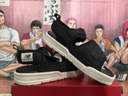 Black New Balance sandals shown from the side at an angle, highlighting the adjustable straps, rear pull tabs, and layered off-white soles.