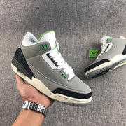 Handheld three-quarter view of a gray Air Jordan 3 sneaker with black, white, and green accents.