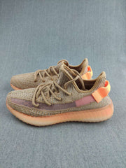 Side view of tan low-top sneakers with tonal laces, a mauve stripe, orange heel details, and textured uppers.