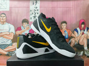 Pair of black Nike basketball sneakers with gold Swoosh accents and white speckled midsoles, displayed on a black box.