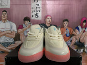 Front view of the beige Jordan sneakers showing perforated toe areas, laces, teal tongue logos, and pink-tinted outsole edges.
