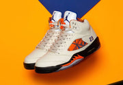Pair of white Jordan Air Jordan 5 high-top sneakers with orange and blue patterned panels on an orange and blue background.