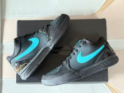 Top-down view of the pair arranged on a black shoe box, showing the turquoise side logos, textured overlays, and black laces.