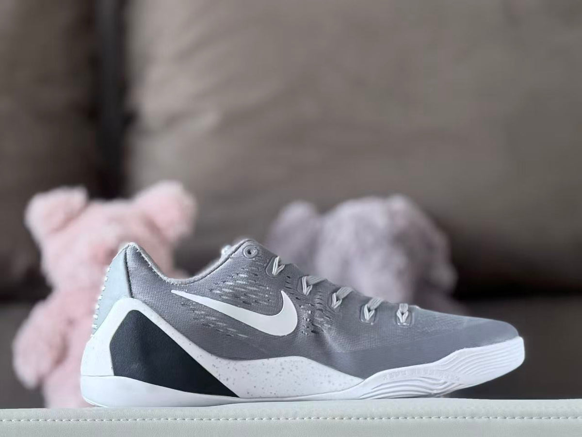 Side view of a grey and white low-top Kobe 9 shoe with dark heel accents.
