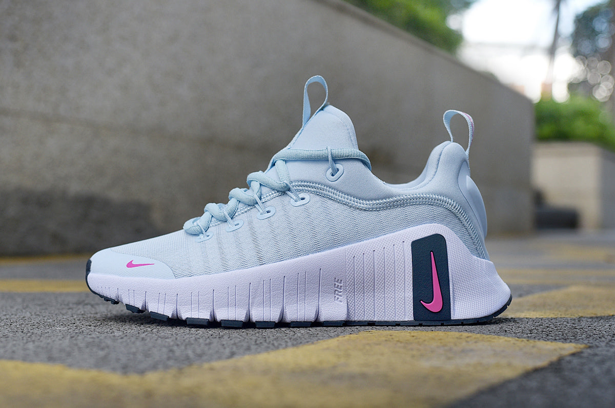 Side view of a light blue Nike running shoe with pink Swoosh accents and a white grooved sole.
