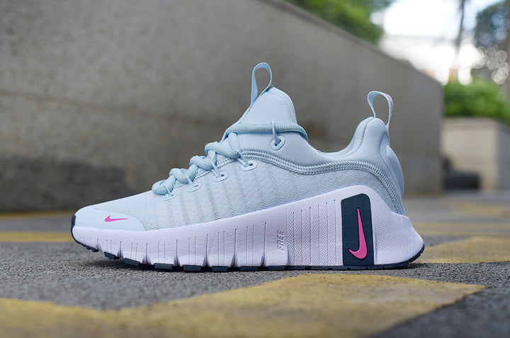Side view of a light blue Nike running shoe with pink Swoosh accents and a white grooved sole.