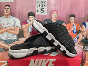Angled view of black Nike slides displaying the open-toe construction, white midsoles, black outsole sections, and side lettering.