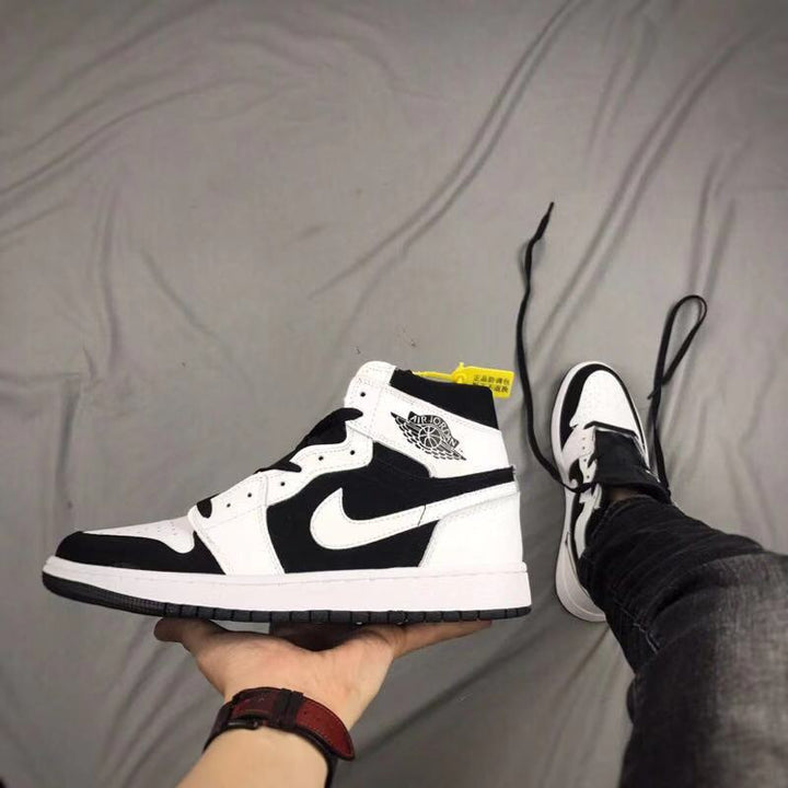 Side view of a black and white high-top Jordan sneaker held above a bed.