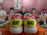 Rear view of pink Nike sneakers with lime-green heel panels, black Nike branding, and white ribbed outsoles.