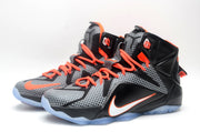 Pair of black and grey Nike high-top basketball sneakers with orange laces and bright orange detailing shown at an angle.