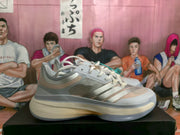 Side profile of an adidas basketball shoe with layered gray and pale blue panels, pink accents, and a cream-colored midsole.