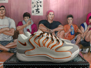 Side profile of a white and grey Nike sneaker with orange piping, a dark swoosh and visible Zoom text on the midsole.