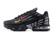 Side profile of a black Nike Air Max Plus sneaker with yellow, pink, and silver-toned accents.