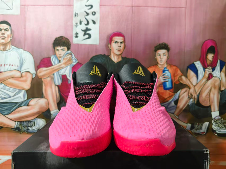 Pair of pink Nike basketball shoes with black tongues and gold tongue emblems, shown from the front.