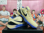 Angled view of beige basketball sneakers with black Swoosh branding, blue trim, laces, and textured upper panels.