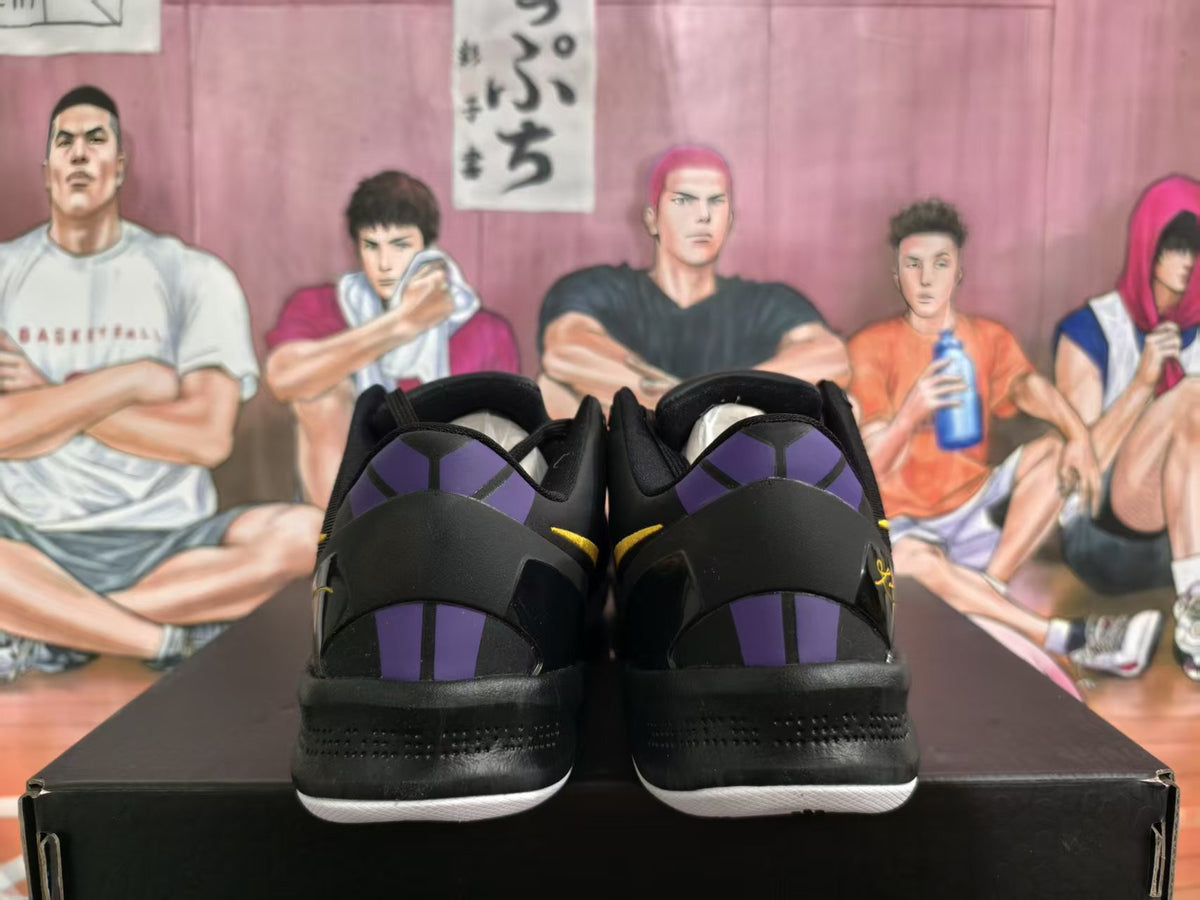 Rear view of black sneakers with purple heel panels, yellow accents, and white outsoles on a black shoebox.