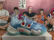 Side view of one blue sneaker showing layered panels, red side accents, a sculpted white midsole, and a translucent outsole.