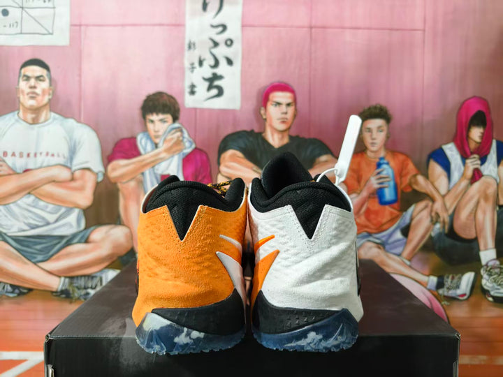 Rear view of white and orange Nike basketball shoes with black collars and translucent-looking outsoles.
