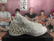 Side profile of a white and light gray Jordan basketball sneaker with patterned upper, gold Jumpman detail, and textured outsole.