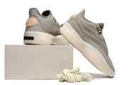 Brown-gray sneakers shown from the rear and side on a light box, highlighting the heel details and cream outsoles.
