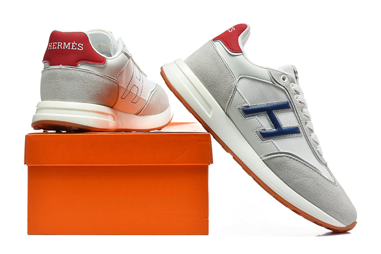 Grey and white low-top sneakers with blue side accents and red heel tabs, shown beside an orange shoebox.