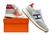 Grey and white low-top sneakers with blue side accents and red heel tabs, shown beside an orange shoebox.