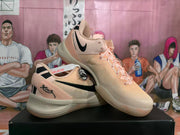 Angled view showing peach-colored basketball shoes with black Swoosh logos and heel graphics.