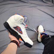 Angled side view of the white sneaker showing its black midsole, orange accent, patterned side panel, and translucent outsole.