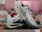 Angled view showing both white and navy Nike basketball sneakers, green heel accents, side branding, and textured outsole details.