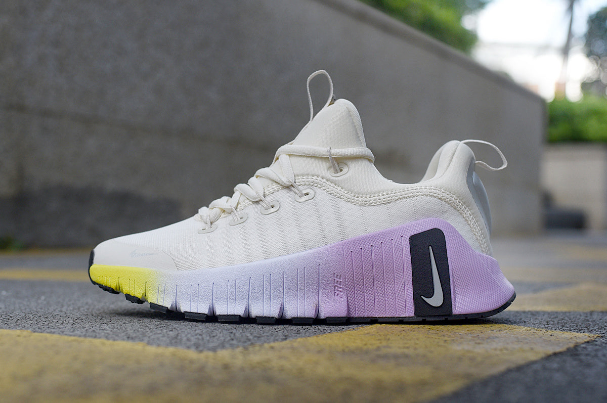 Side view of a light-colored Nike lace-up sneaker with a white, purple, and yellow sculpted sole.