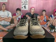 Front view of Nike basketball sneakers showing beige textured uppers, black-and-white patterned laces, white Swoosh branding, and gum-colored outsoles.