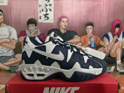 Side view of a white and dark blue Nike sneaker showing the contrasting swoosh, layered upper, and chunky outsole.