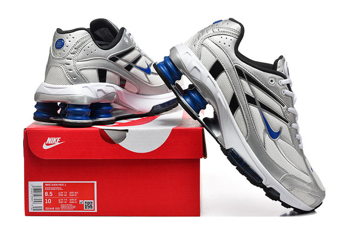 Silver and white Nike Shox Ride 2 sneakers with blue accents displayed on a red shoe box.