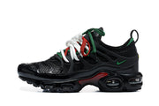 Side view of a black Nike Air Max Plus sneaker with green accents and visible cushioning windows.