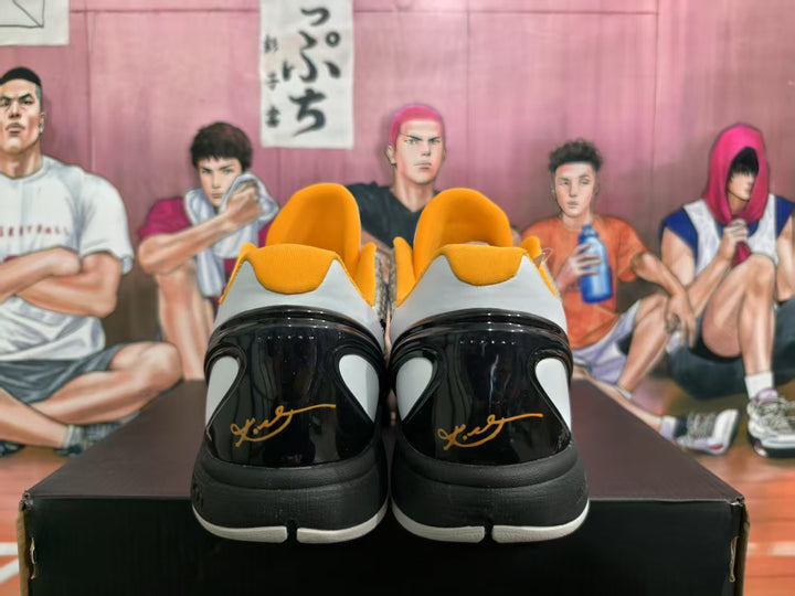 Rear view of the white, black, and gold basketball sneakers showing glossy black heel panels and gold signature-style details.