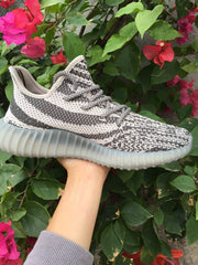 Side profile of one gray and off-white knit sneaker with patterned upper and ribbed sole.