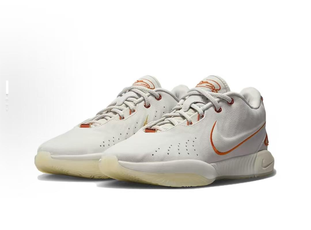 White low-top Nike basketball shoes with orange accents, shown as a pair.
