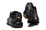 Black Nike Air Max Plus sneakers viewed from the heel and outsole, showing TN badges and yellow outsole accents.