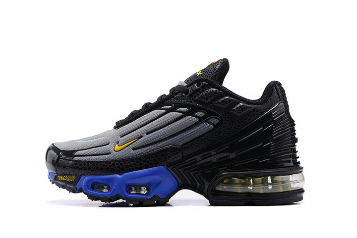 Side view of black and grey Nike Air Max Plus TN sneakers with a yellow Swoosh and blue midsole accents.