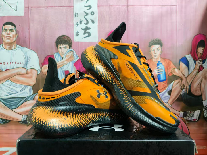 Orange and black Under Armour basketball sneakers displayed on a black box from an angled side view.