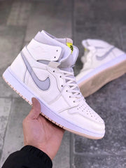 Front three-quarter view of the pearl white high-top sneaker showing perforated toe panels, white laces, and yellow tongue label.