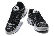 Front angled view of a pair of black and grey Nike Air Max Plus sneakers with black laces