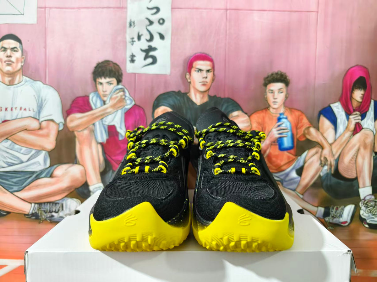 Pair of black and yellow basketball sneakers shown from the front on a white box.