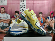 Angled view of two Nike basketball sneakers showing lime mesh, white panels, gold detailing, blue accents, and translucent soles.