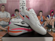 White Nike basketball shoes shown from the side and at an angle, with black Swoosh accents and pink and orange details.