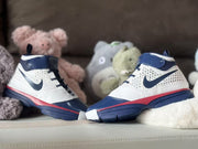 Side profile of the high-top sneakers with navy outsoles, white uppers, red trim, and dark swoosh details.