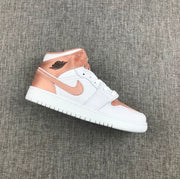 Side view of a white and rose-gold Air Jordan 1 Mid sneaker on a gray fabric background.